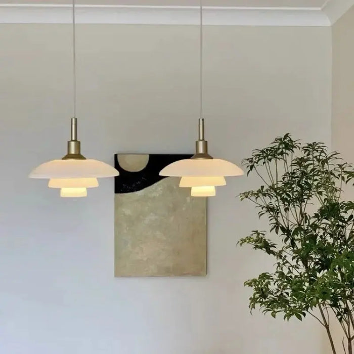 Two pendant lights hanging from the ceiling with a plant and abstract art in the background.